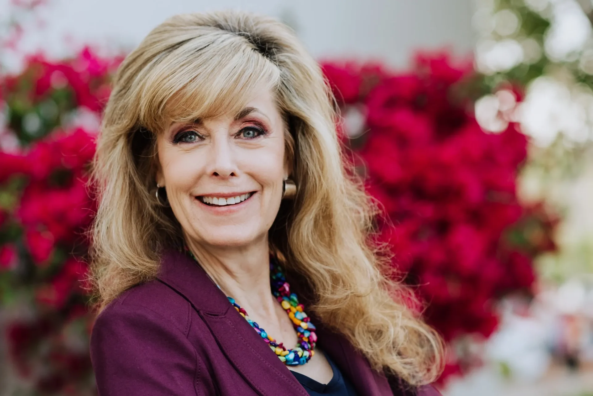 A woman with long blonde hair wearing a purple jacket.