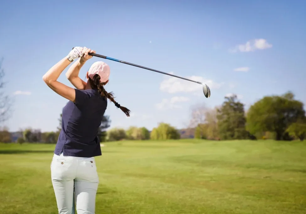 A woman swinging at a golf ball on the course.