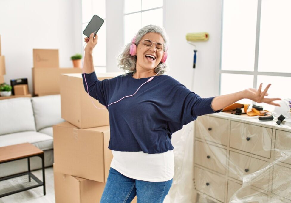 Middle age grey-haired woman smiling happy dancing at new home.