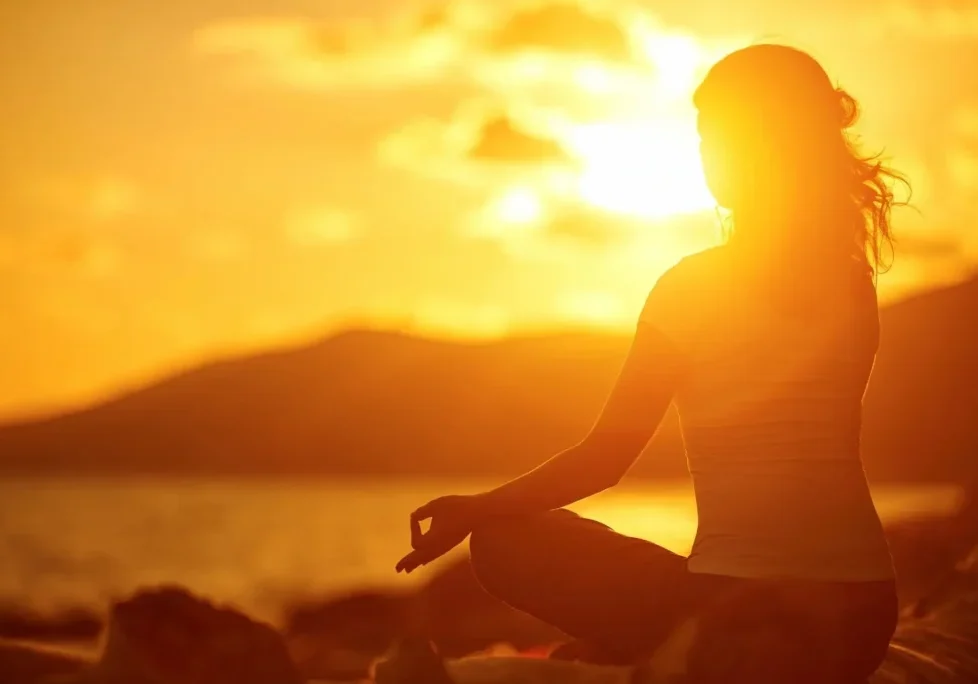 A person sitting in the sun with their hands in yoga pose.